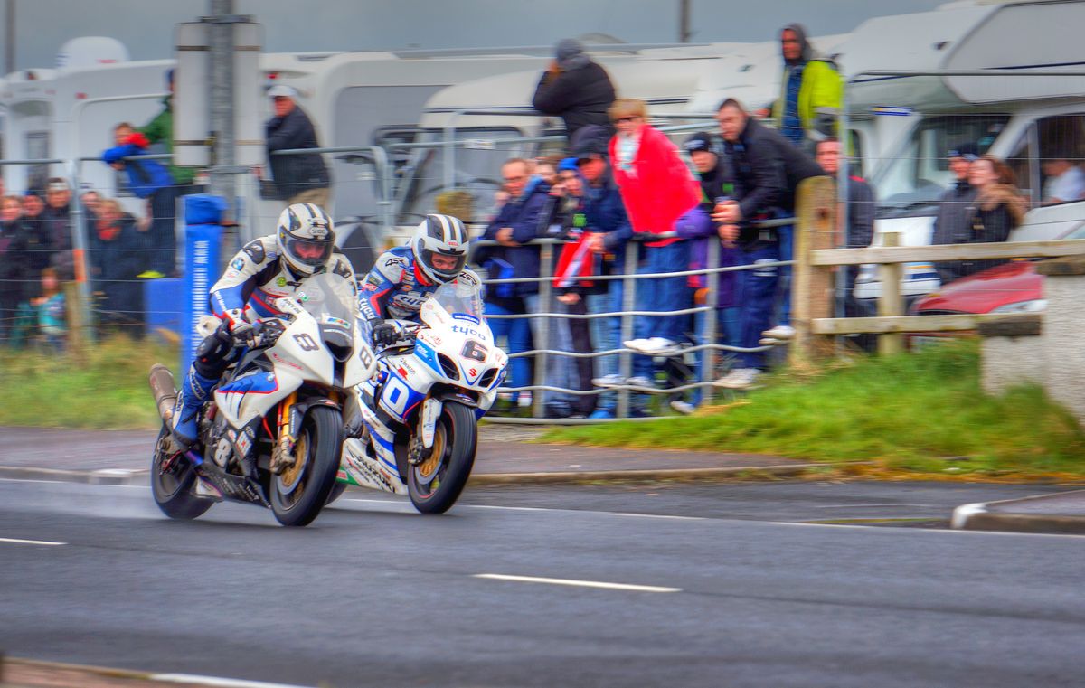 Taken at the North West 200 Road Races in Portrush, N Ireland.  The race takes place on closed public roads inches from kerbs, walls and telegraph poles at speeds of up to 200 mph.  The photo shows brothers William and Michael Dunlop fighing for the lead of the superbike race.