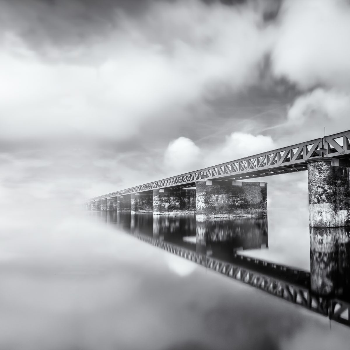 reflectie van een oude treinbrug in het water, met een mooie wolkenlucht